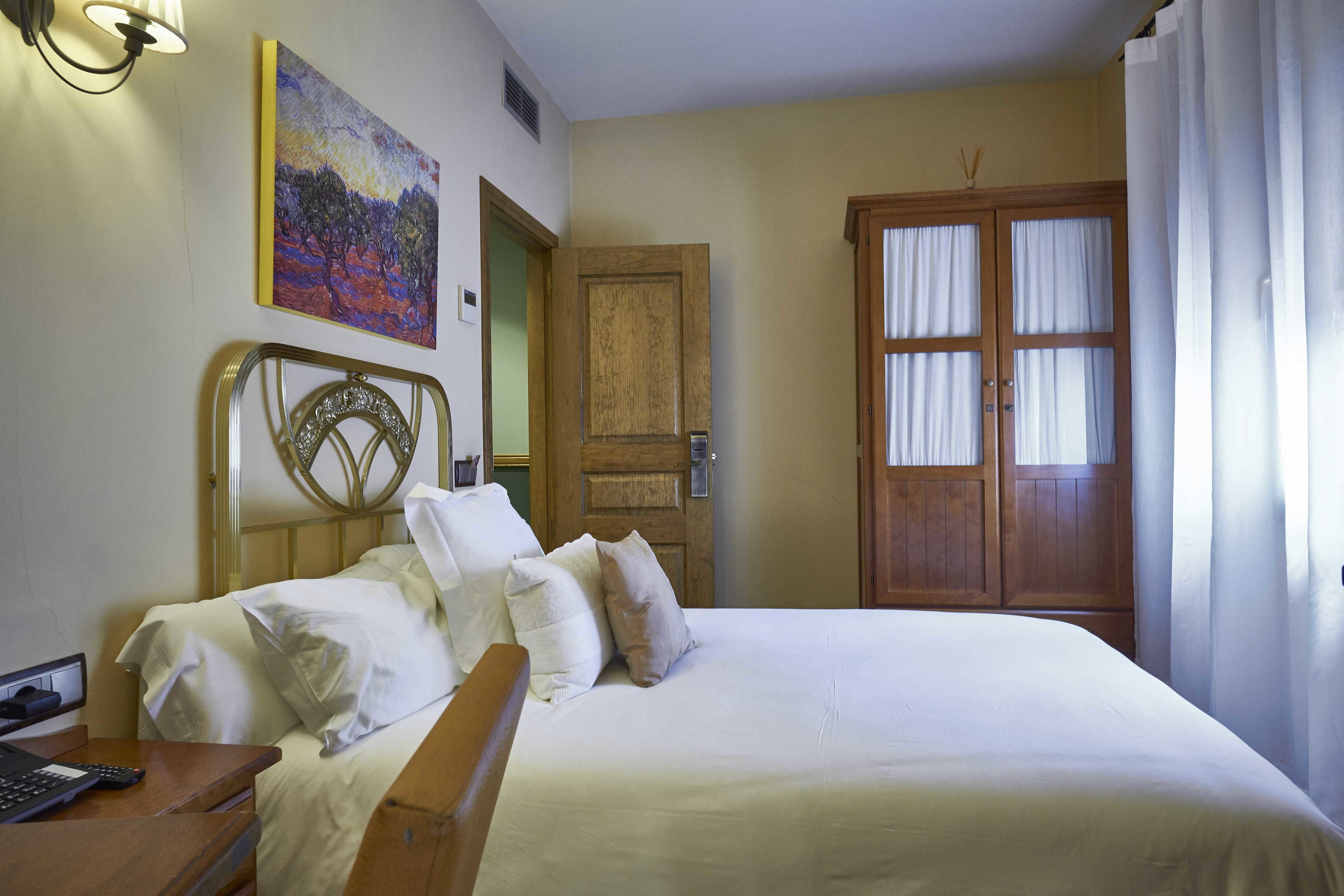 Una cama bien hecha con sábanas blancas y varias almohadas, un cabecero de madera, un cuadro en la pared y una puerta de madera con cortinas.