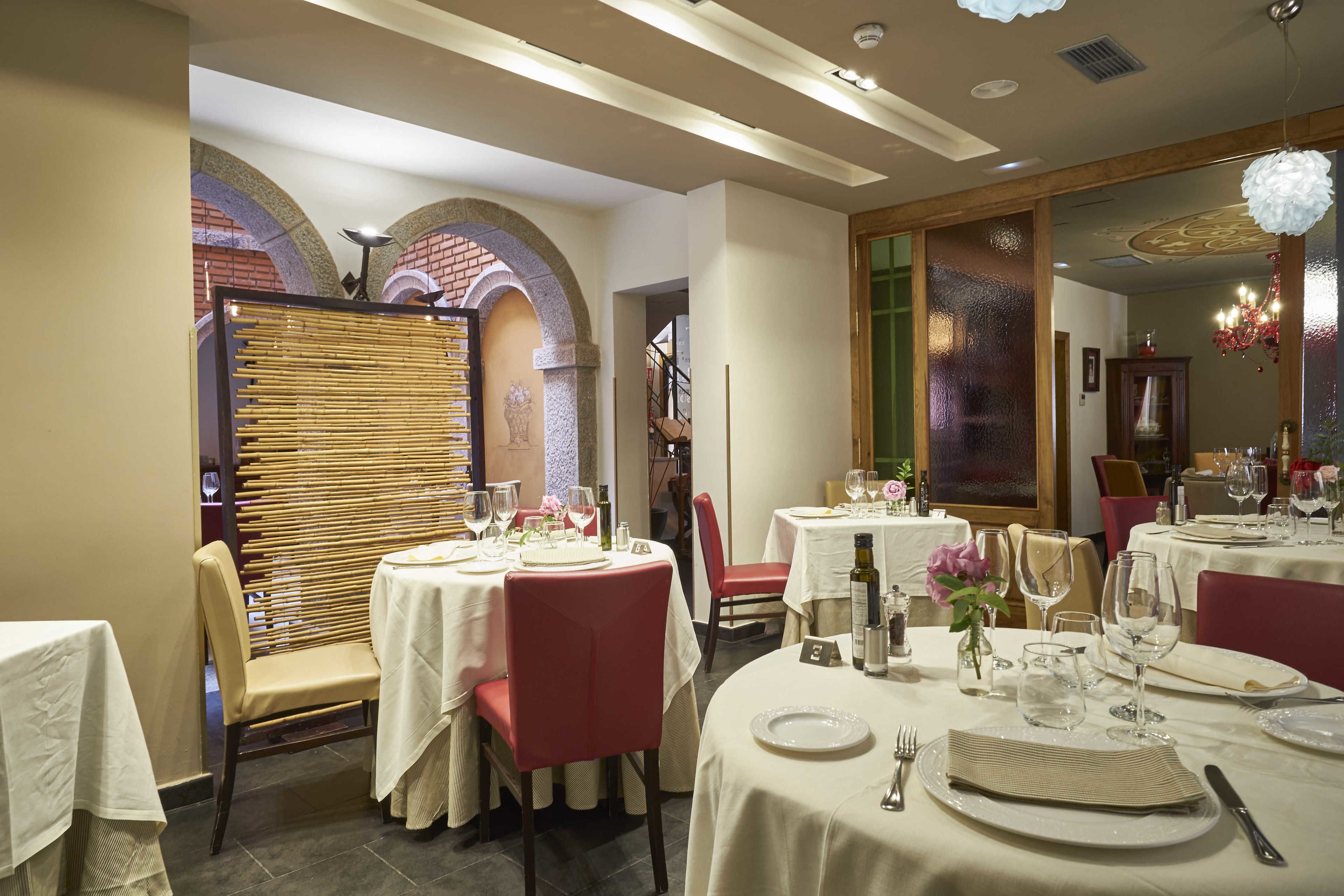 Un área de comedor con mesas redondas, sillas rojas y manteles blancos.