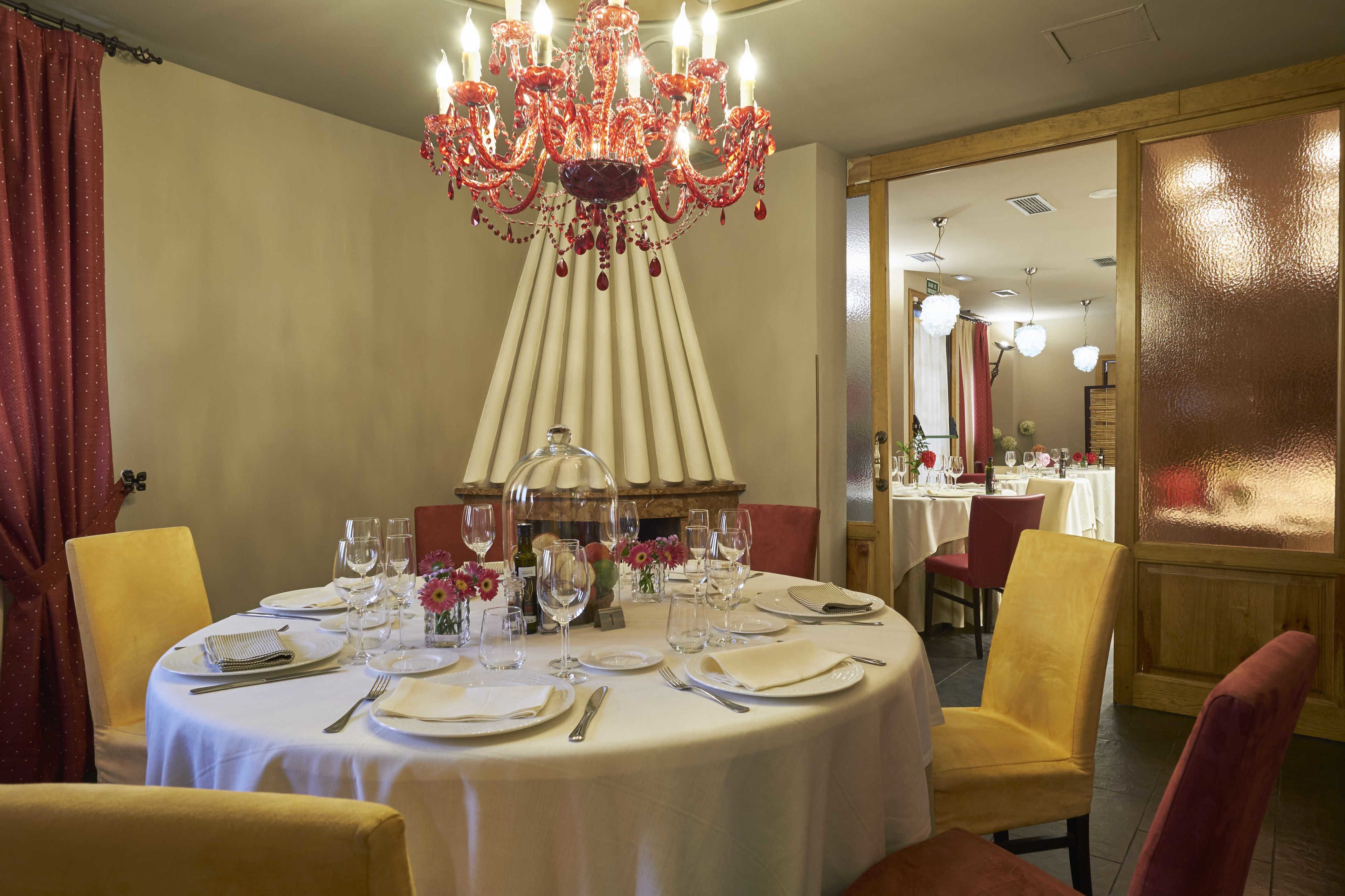 A dining area with a round table set for four, white tablecloths, and a red chandelier.
