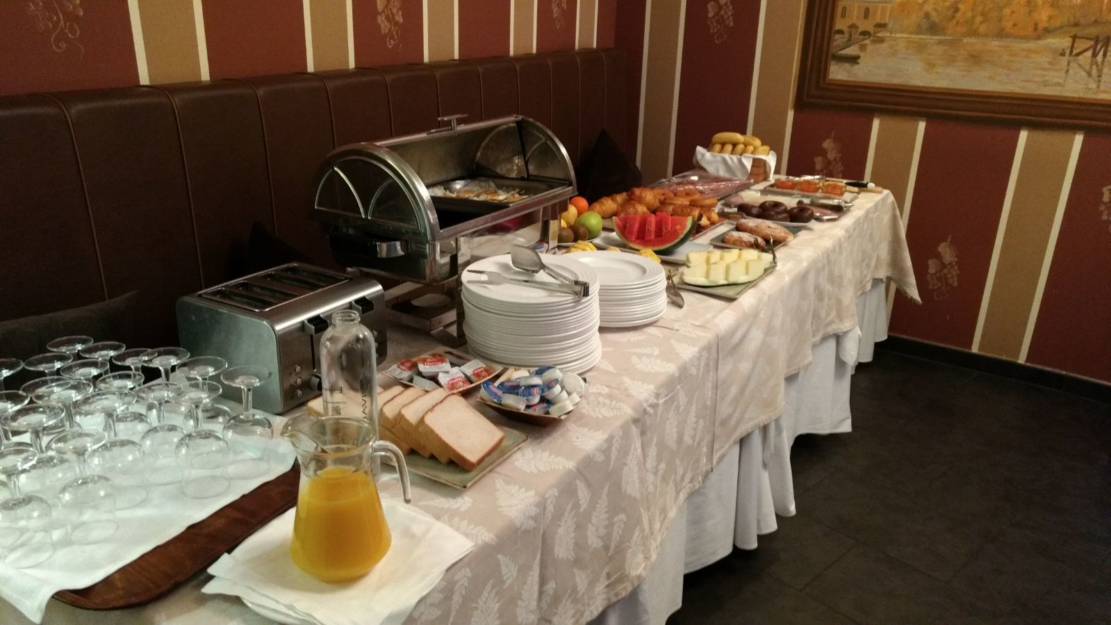 Ein reichhaltiges Buffet mit verschiedenen Speisen, einem Saftkrug und gestapelten Tellern.