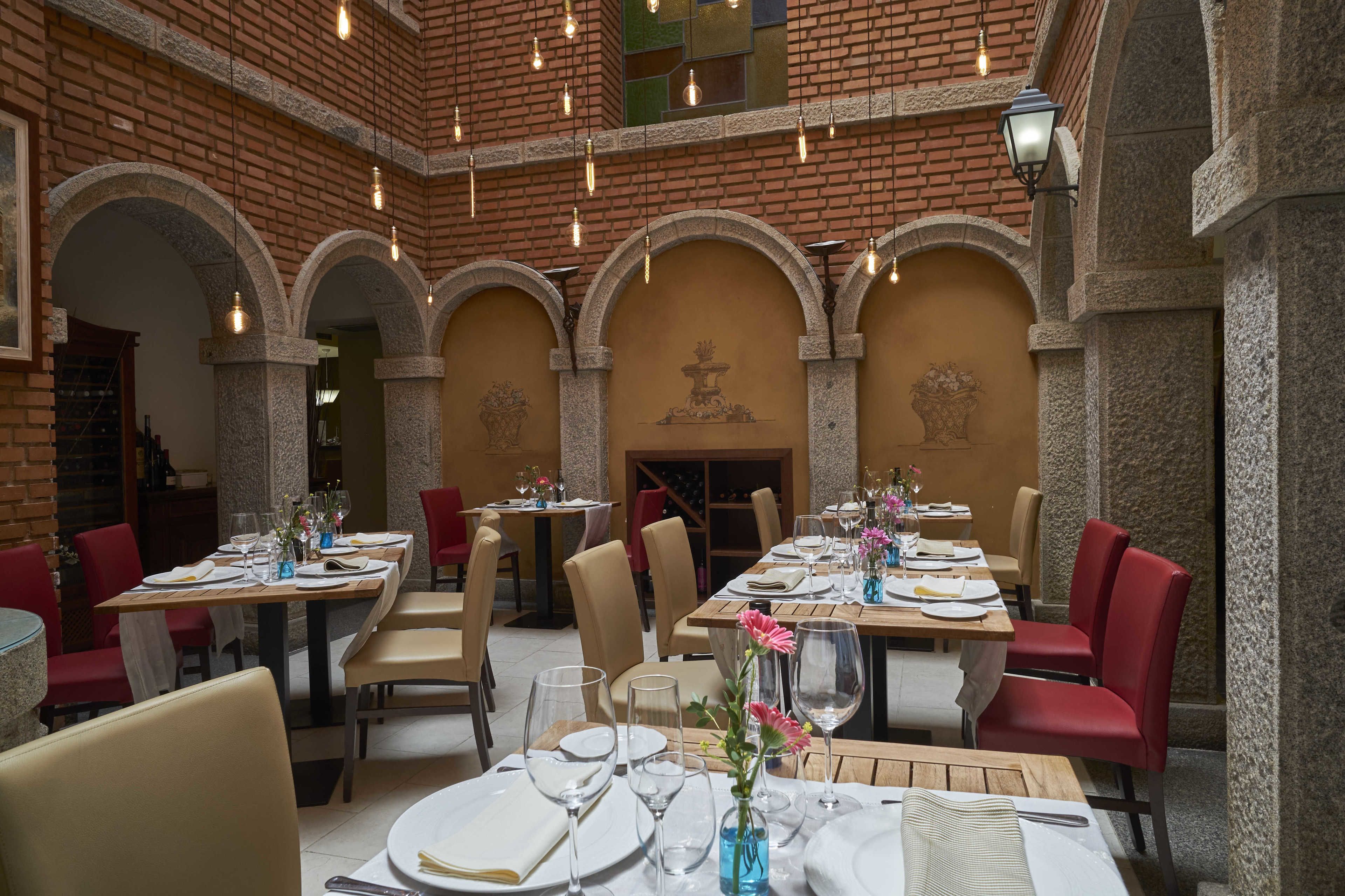 A restaurant with brick walls, arched ceilings, and multiple dining tables set with white tablecloths and red chairs.