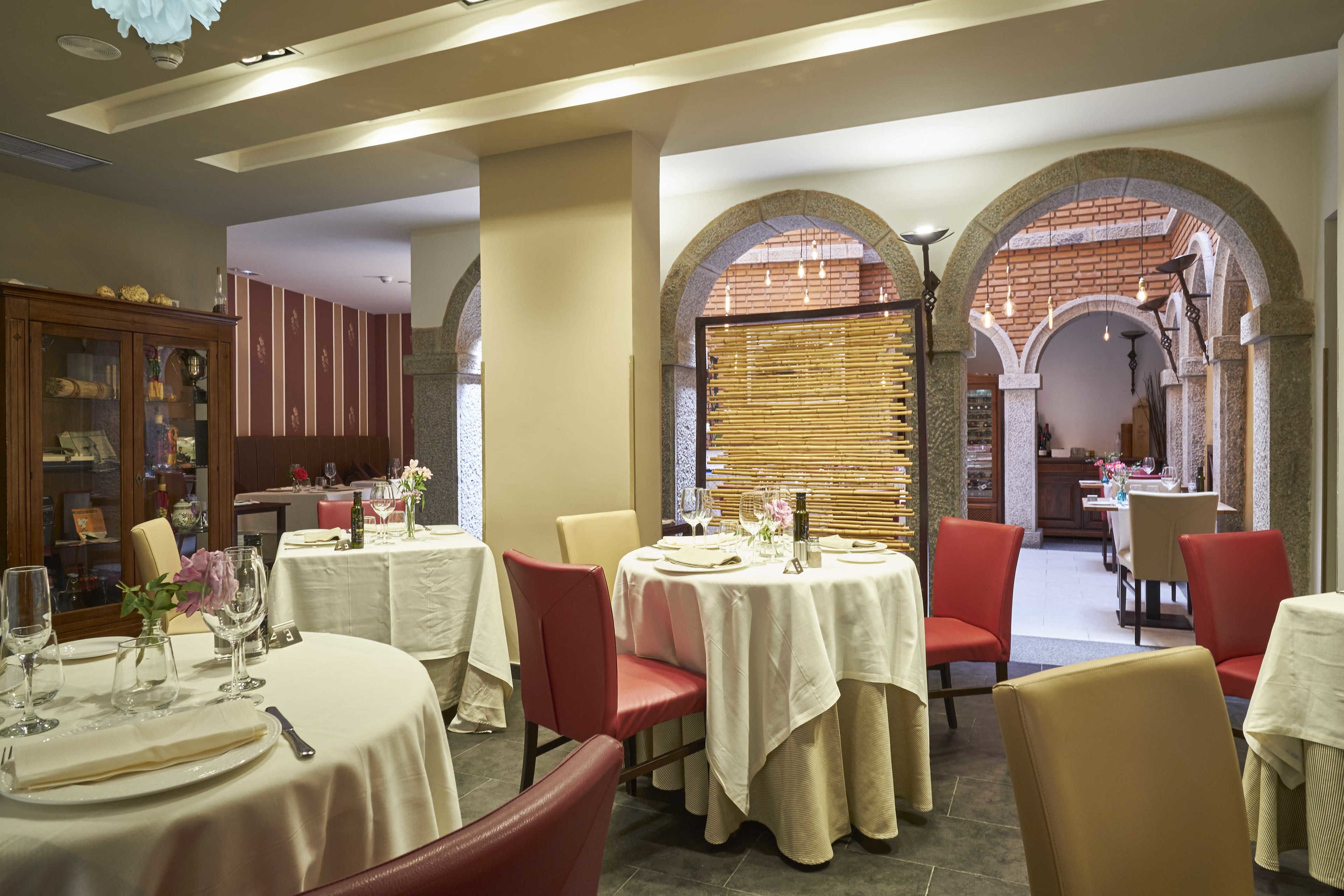 Un restaurante con mesas redondas, sillas rojas y una pared de ladrillo al fondo.