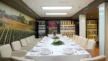 A dining area with a long table set for a meal, surrounded by chairs. There are wine bottles displayed on shelves in the background.