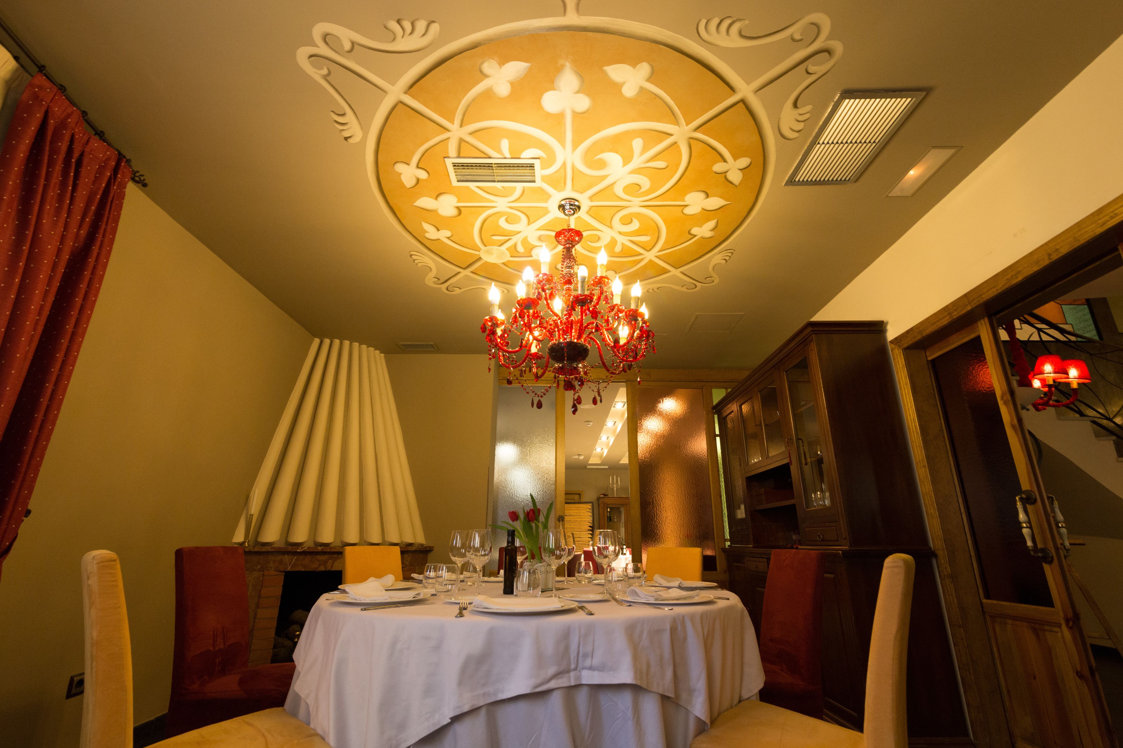 Un comedor con una mesa redonda dispuesta para una comida, una araña y un espejo que refleja la habitación.