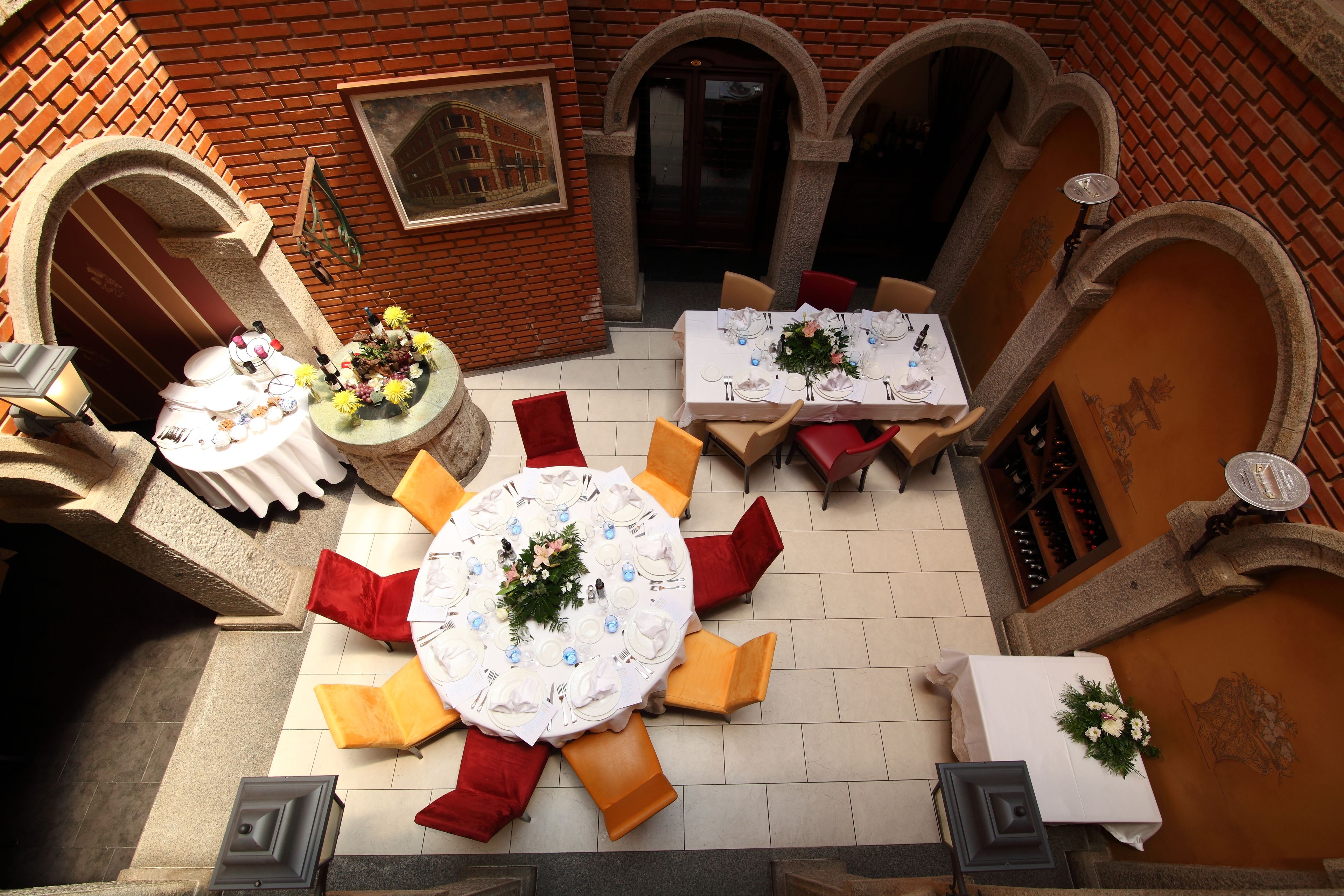 Un área de comedor al aire libre con mesas y sillas redondas, frente a una pared de ladrillo con arcos.