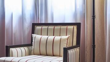 Une chaise recouverte d’un tissu à rayures, accompagnée d’un coussin assorti, placée devant une fenêtre ornée de rideaux légers.