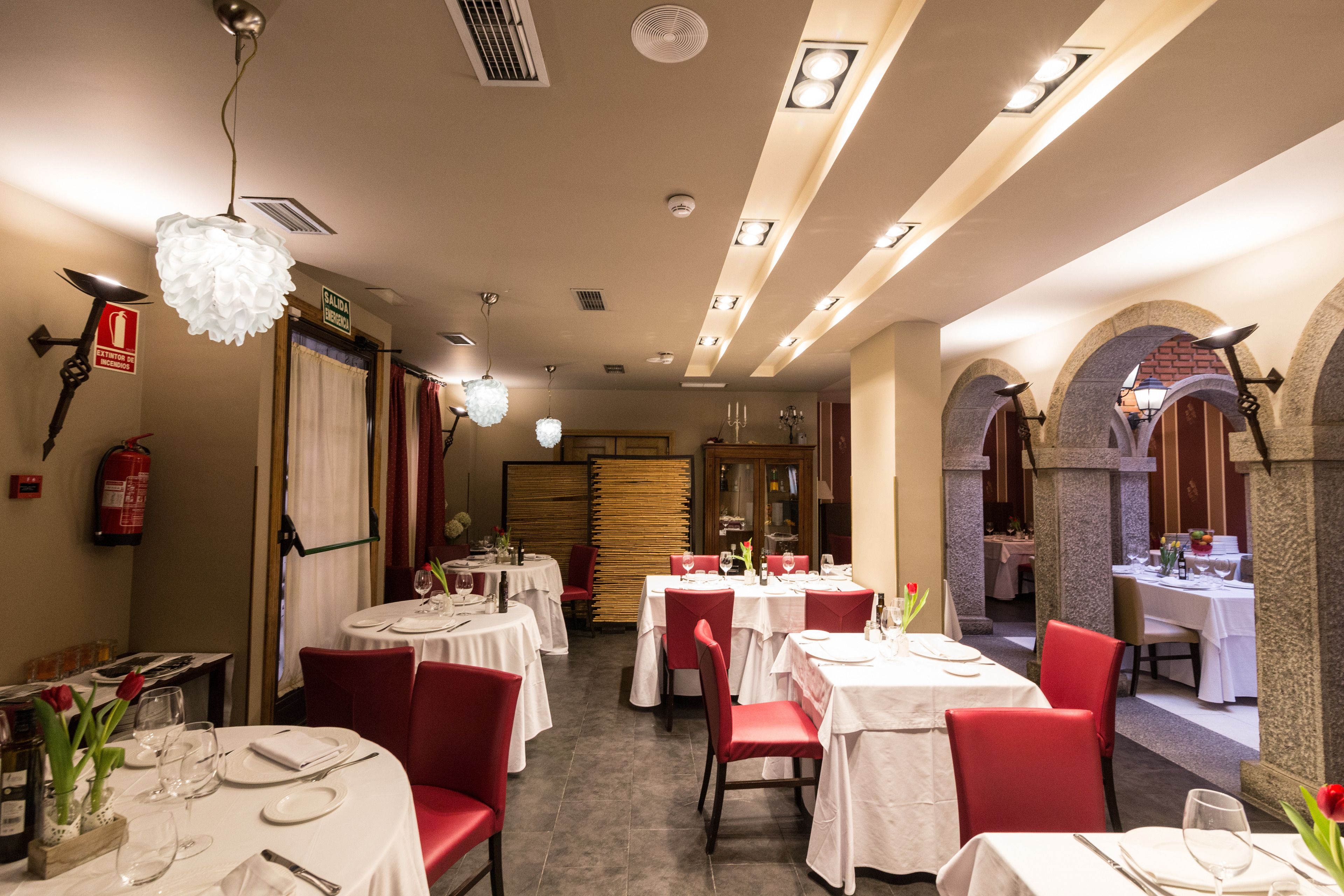 Un restaurante con mesas redondas, sillas rojas y manteles blancos.