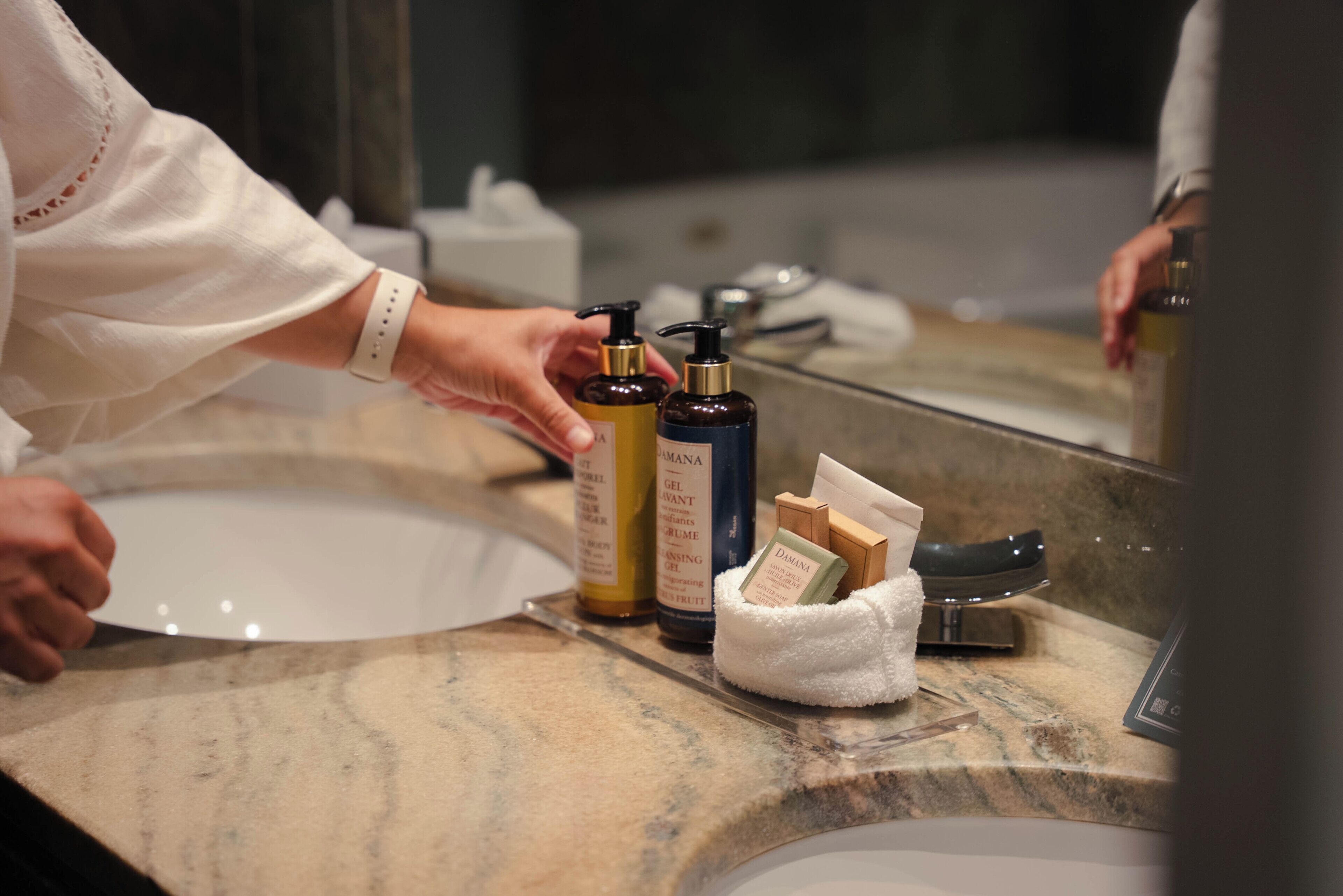 A bathroom with a marble sink, a mirror, and toiletries including a soap dispenser and a bottle of shampoo.