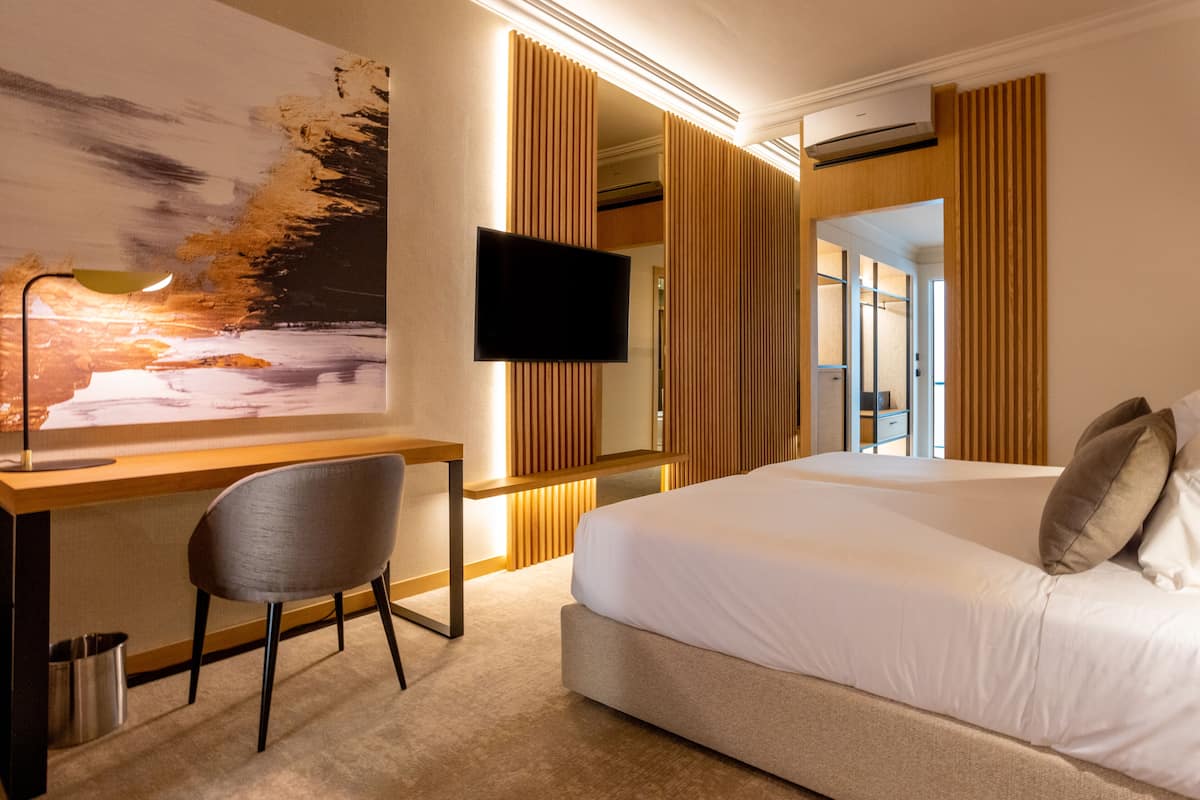 A modern hotel room with a large bed, a desk with a chair, a flat-screen TV, and a large abstract painting on the wall.