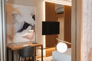 Una habitación de hotel moderna con escritorio, silla, televisor de pantalla plana, obras de arte y lámpara de noche.