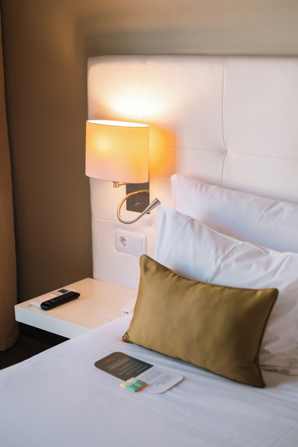 A hotel room with a bed, a bedside table, a remote control, and a lamp.