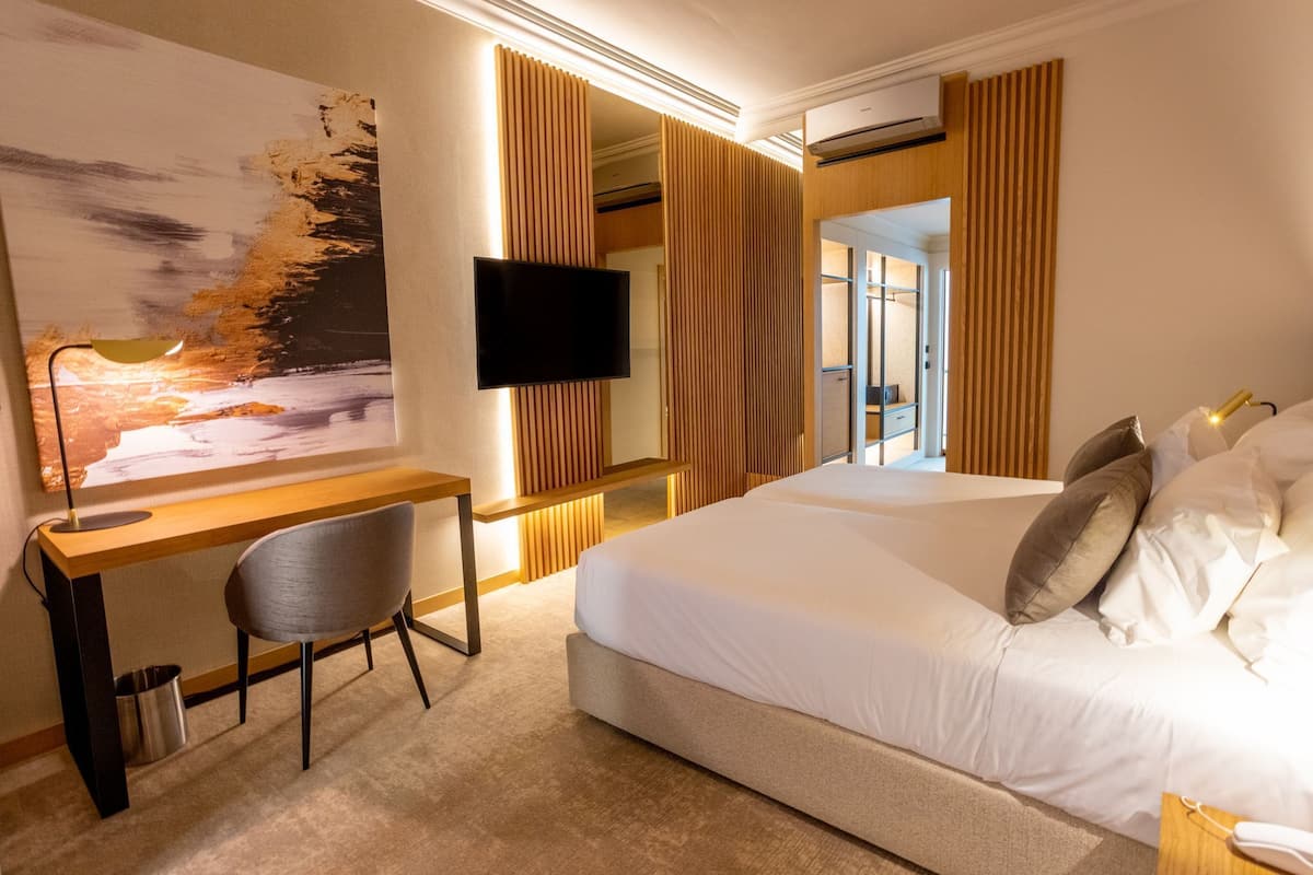 A hotel room with a bed, a desk, a chair, a TV, and a large painting on the wall.