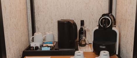 A hotel room's minibar with a coffee maker, a bottle of wine, and a pair of headphones.