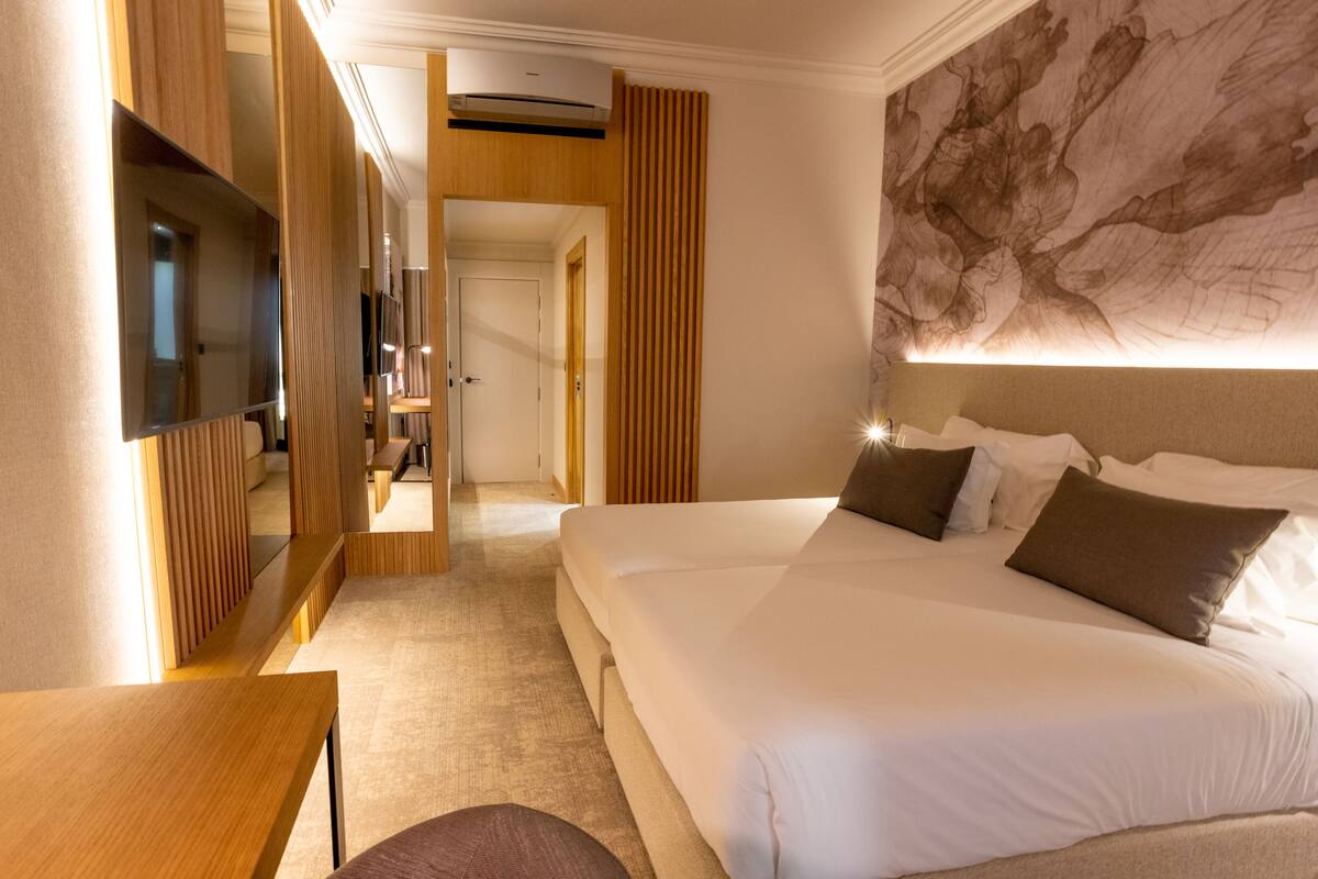 A hotel room with a large bed, a flat-screen TV, a wooden desk, and a large abstract painting on the wall.
