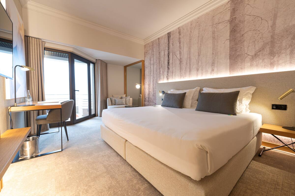 A spacious hotel room with a large bed, a desk, and a chair.