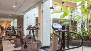 Un gimnasio con bicicletas estáticas, cintas de correr, una pared de vidrio y plantas de interior.