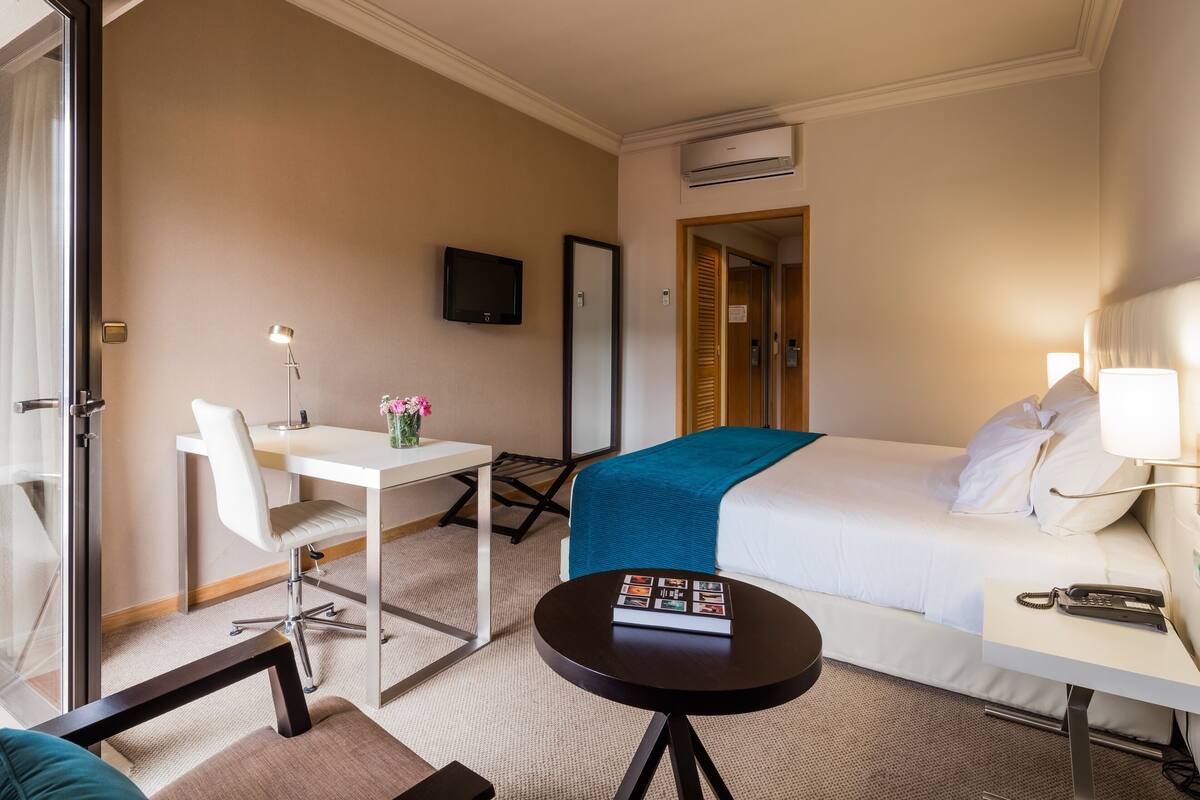 A hotel room with a bed, bedside table, desk, chair, and a television on the wall.