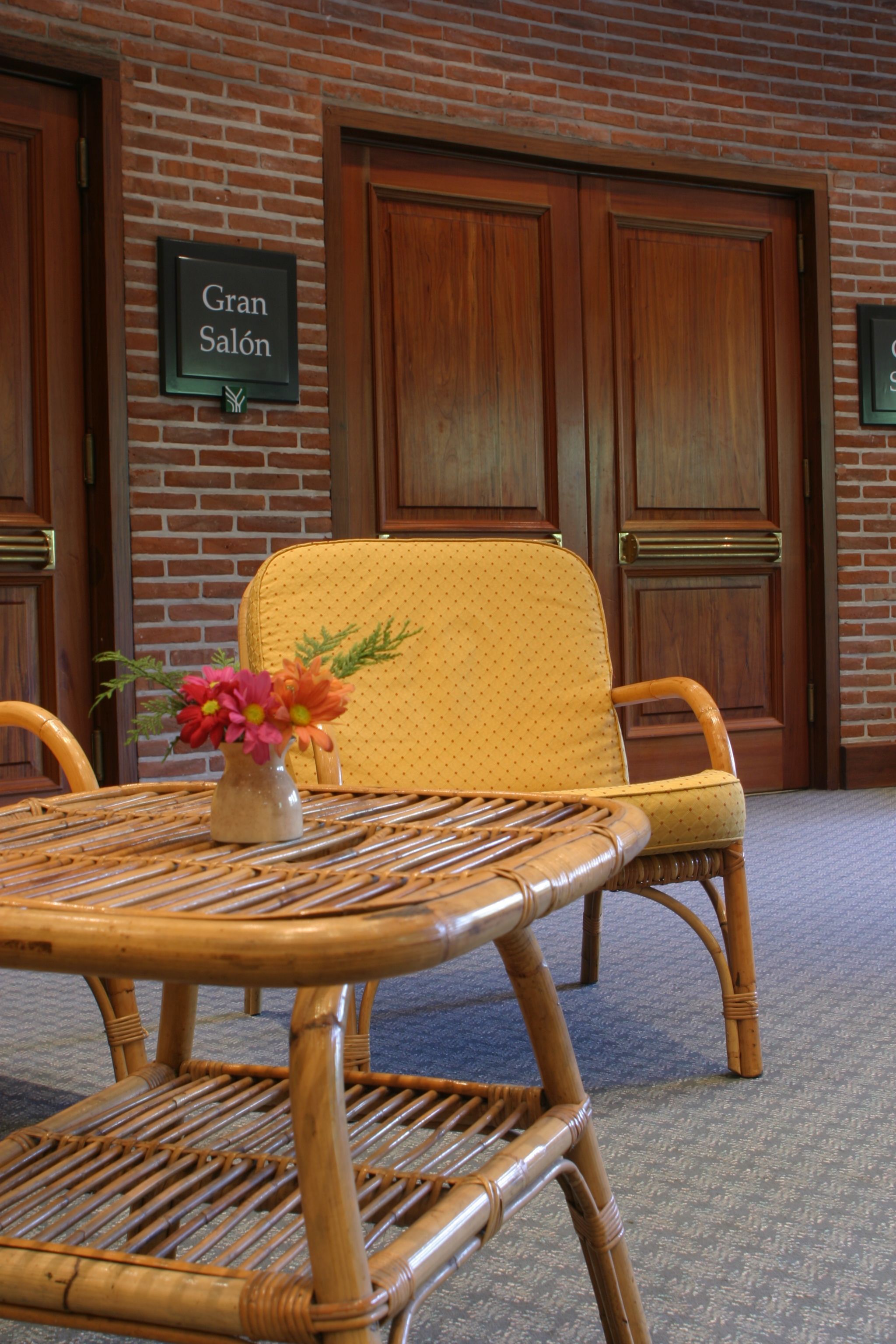 A wicker chair and table set against a brick wall with a sign reading "Gran Salón".