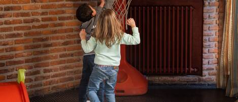 Des enfants jouent dans un parc, avec un mur de briques et une fenêtre en arrière-plan.