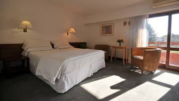 Habitación de hotel con cama, mesitas de noche, una silla, una pequeña mesa y una ventana con cortinas.