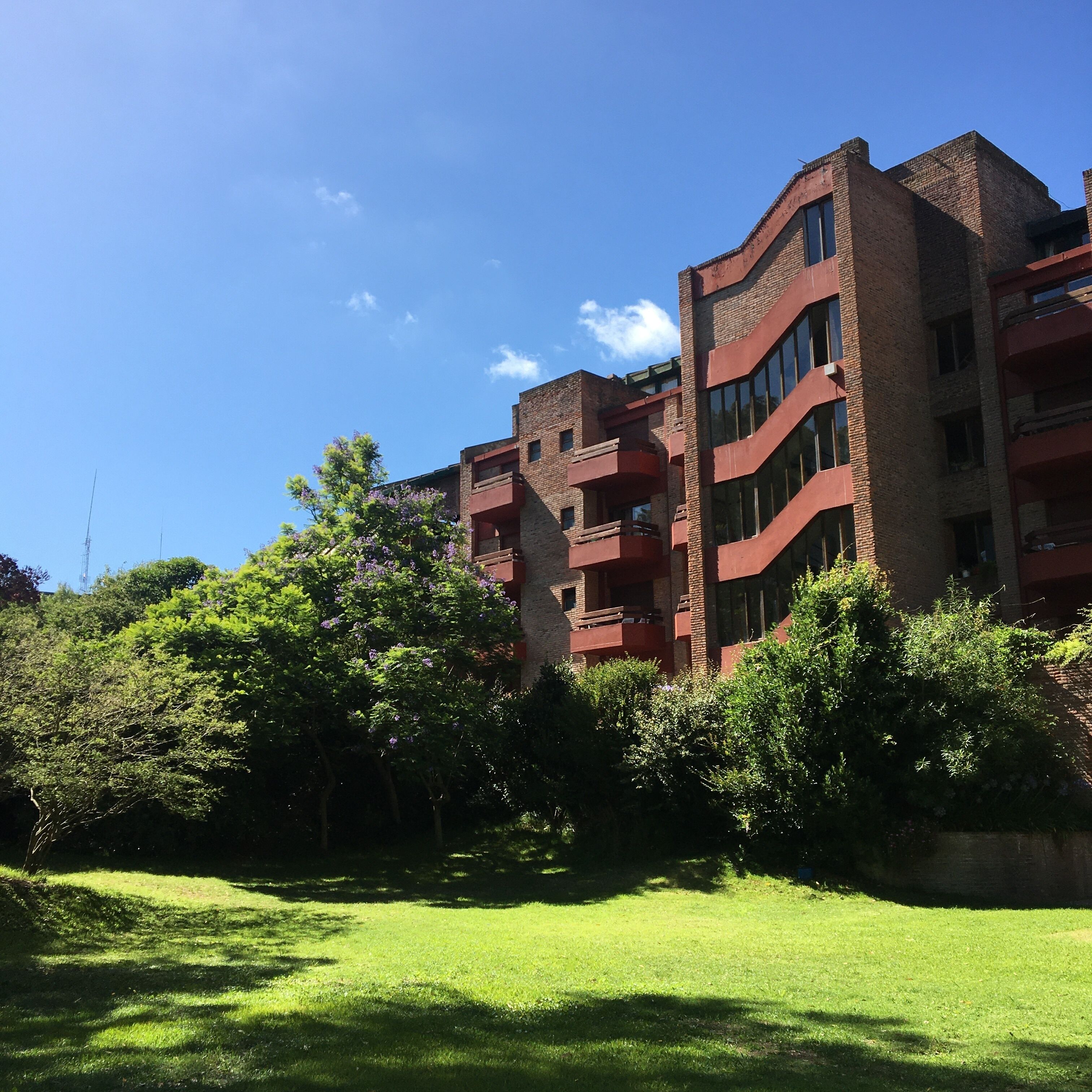 Un edificio de varios pisos con fachada de ladrillo, balcones y un área verde al frente.