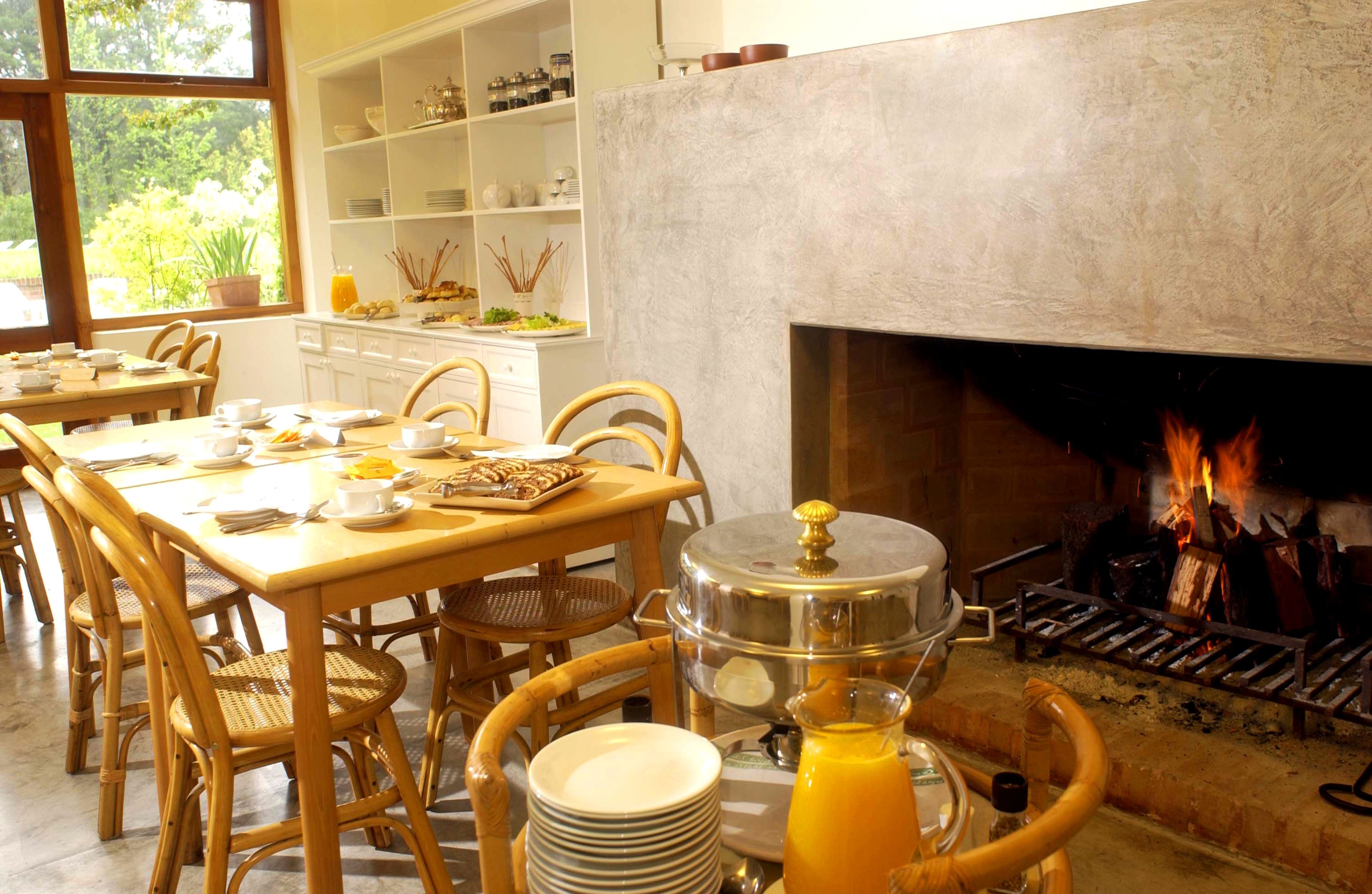 Un ambiente de desayuno con bufé, sillas de madera, chimenea y vistas al exterior con vegetación.