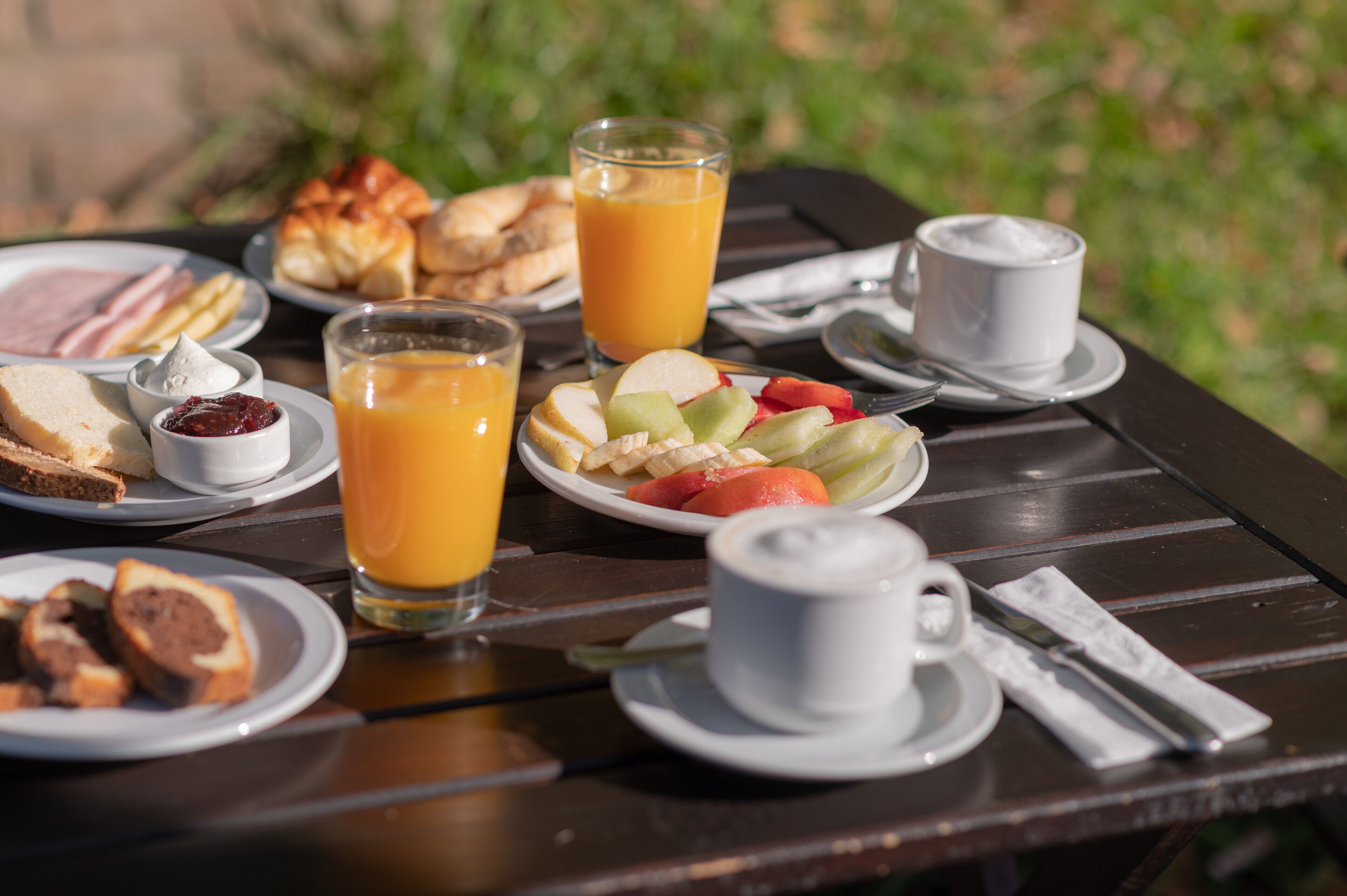 Une table de petit-déjeuner avec des assiettes remplies de nourriture, des verres de jus d’orange et une tasse de café.