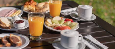 Une table de petit-déjeuner avec des assiettes remplies de nourriture, des verres de jus d’orange et une tasse de café.