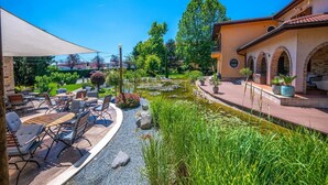 An outdoor patio with tables and chairs, a small pond with lily pads, and a building with arched windows.