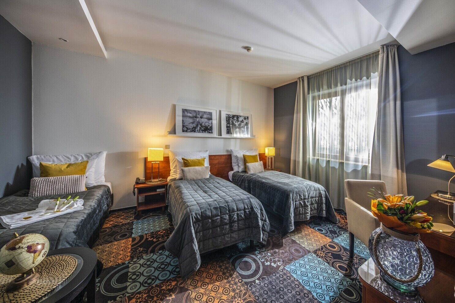 A hotel room with two beds, a desk, a chair, and a large window with curtains.