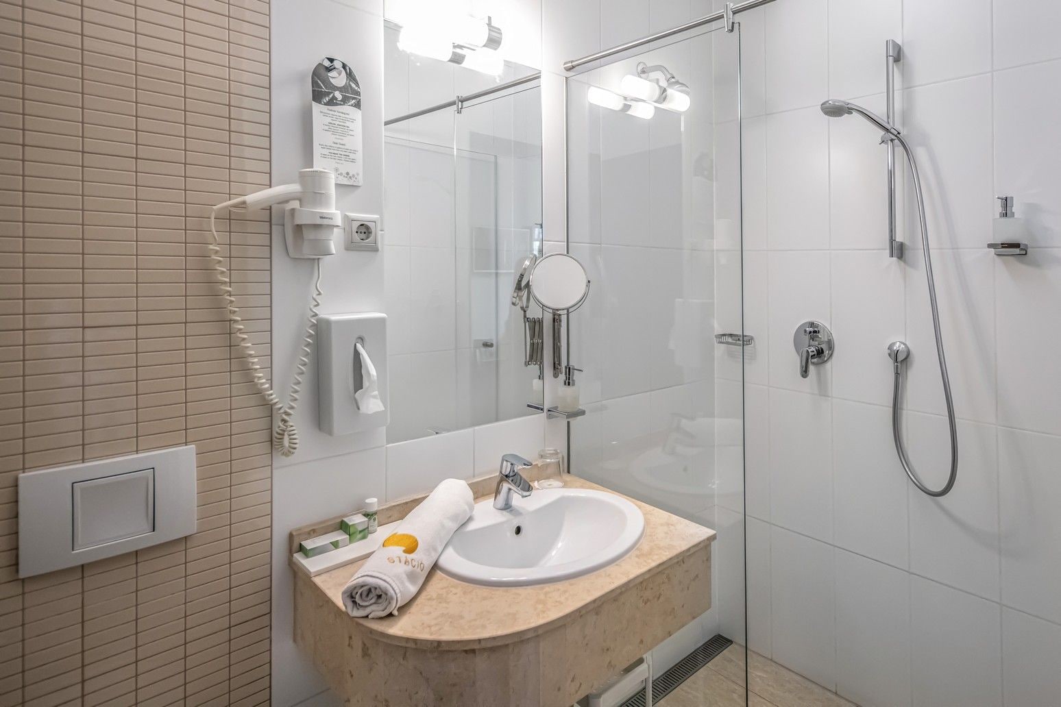 Un baño moderno con ducha envuelta en vidrio, un lavamanos blanco y una toalla sobre el mostrador.