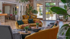 A spacious lobby with a yellow sofa set, a grey armchair, and a coffee table with a vase of flowers.