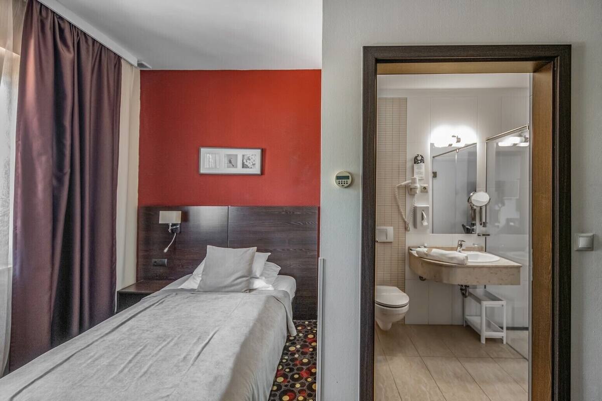 A hotel room with a bed, a nightstand, a wall-mounted phone, and a red accent wall.