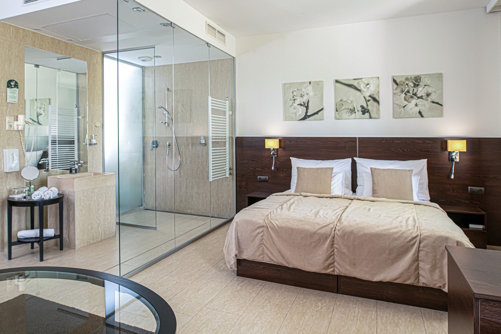 Een moderne hotelkamer met een douchecabine van glas, een bed met houten hoofdbord en kunst aan de muur.