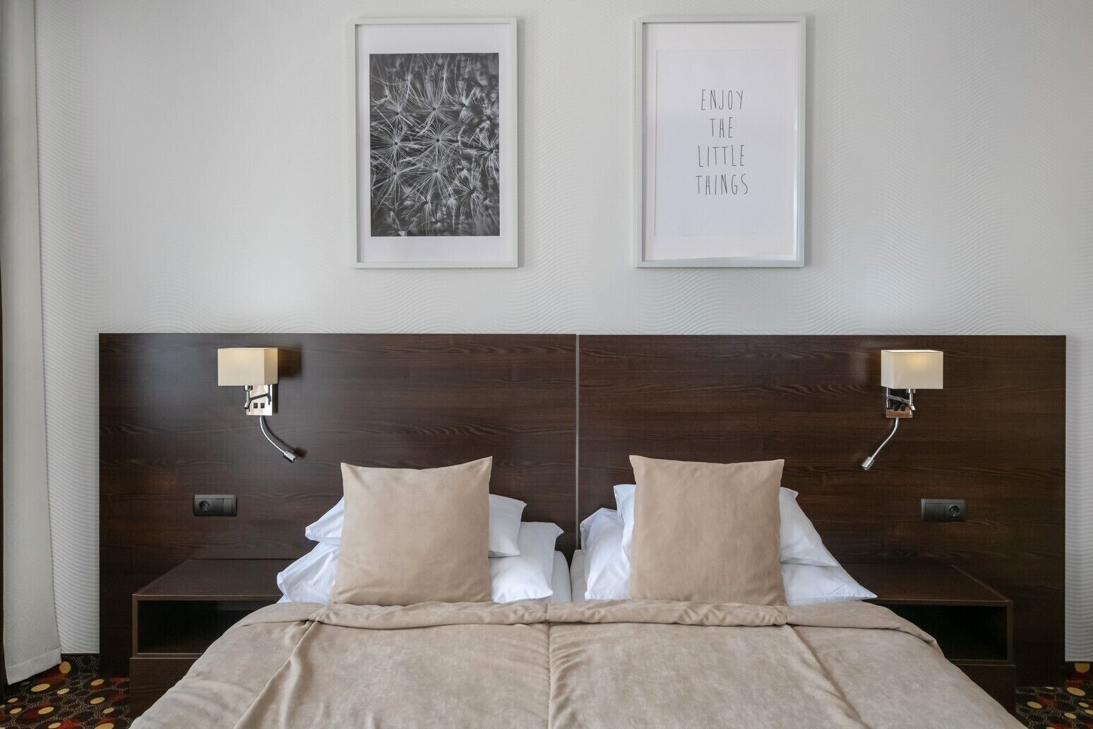 Habitación de hotel con una cama grande, dos mesitas de noche, dos lámparas de pared y dos cuadros enmarcados.