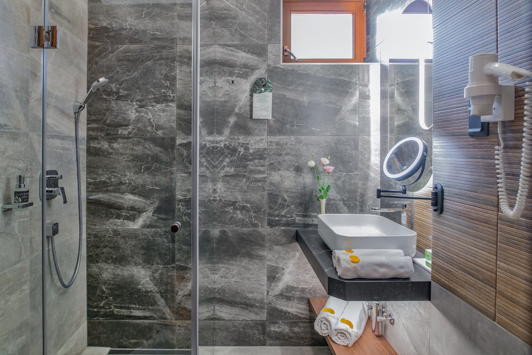Un baño moderno con ducha de vidrio, lavabo con espejo y tocador de madera.