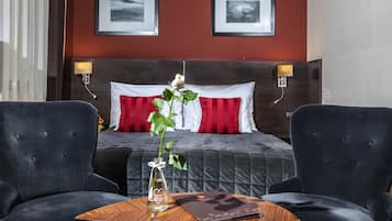 Una habitación de hotel con una cama grande, dos lámparas de noche, un jarrón con una flor y dos sillones.