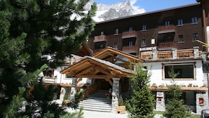 Un hotel con fachada de madera, detalles de piedra y un paisaje montañoso al fondo.