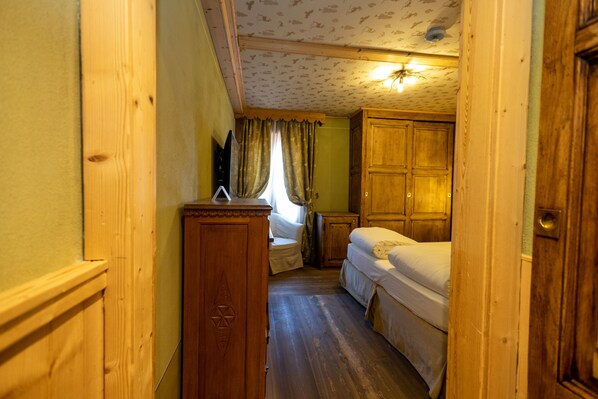 A narrow hallway leading to a bedroom with a wooden wardrobe, a bedside table, and a bed.