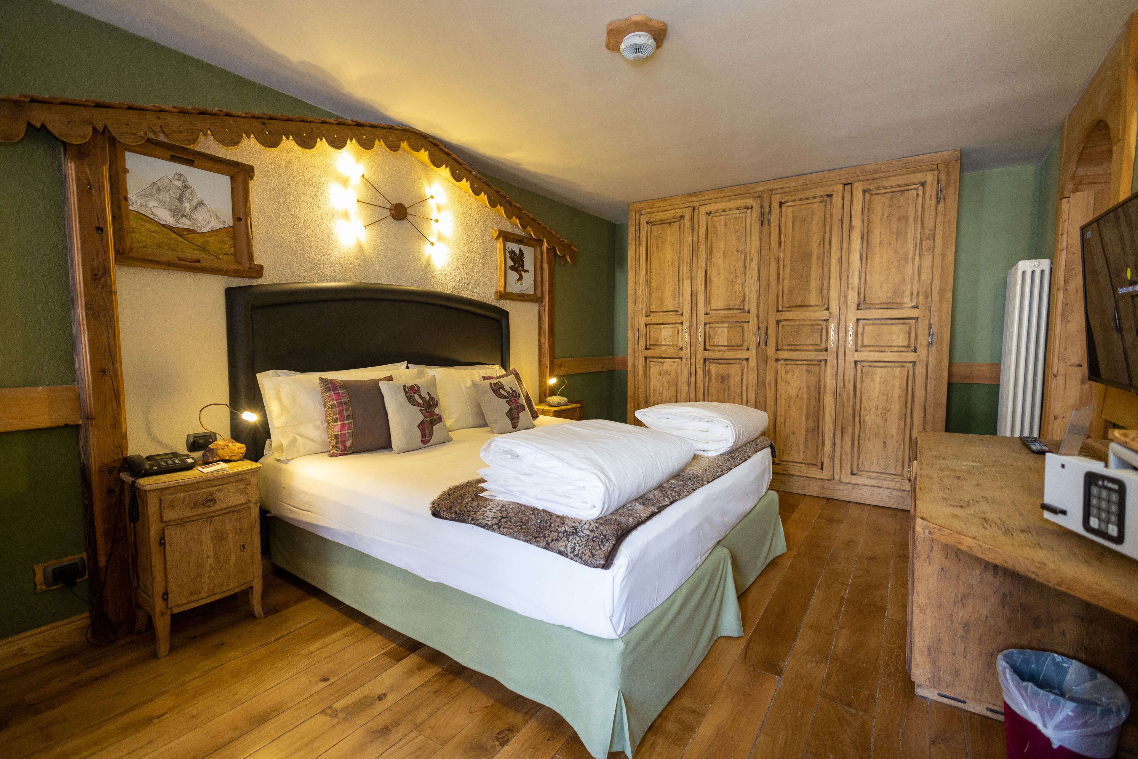 A bedroom with a large bed, wooden wardrobe, and a small bedside table with a lamp.