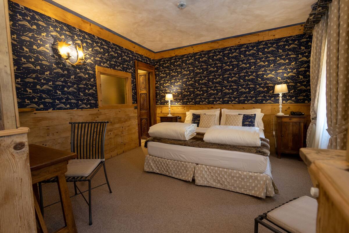 Una habitación con una cama, dos mesitas de noche, una silla, un escritorio de madera y un espejo.