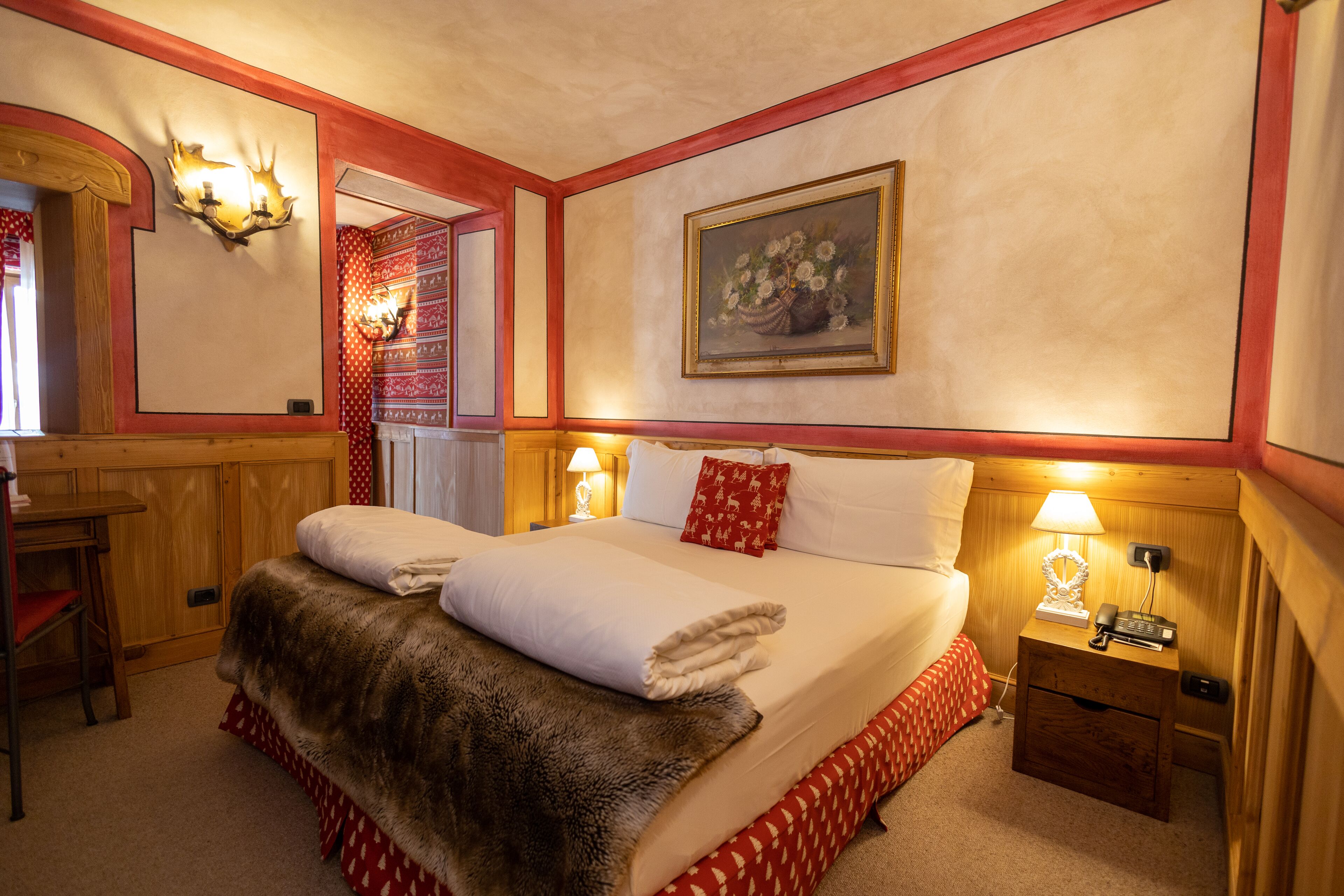 A neatly made bed with a fur throw, a painting on the wall, and a nightstand with a lamp and phone.