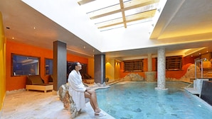 Una persona sentada junto a una piscina en un espacio interior moderno con suelo de piedra y paredes anaranjadas.