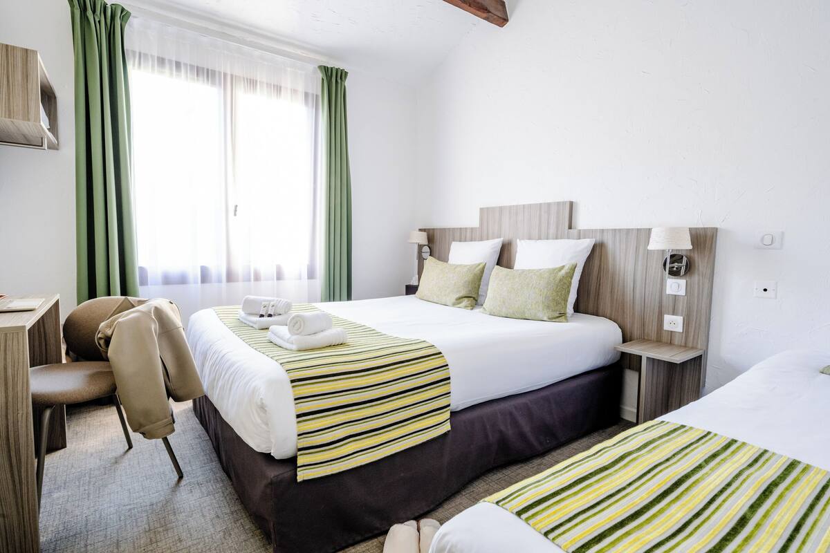 A hotel room with two beds, a desk, and a chair.