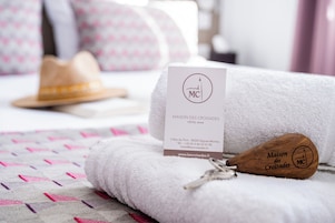 Habitación de hotel con una toalla blanca doblada con cuidado, un bastón de madera con el logotipo del hotel y una tarjeta de presentación sobre la toalla.