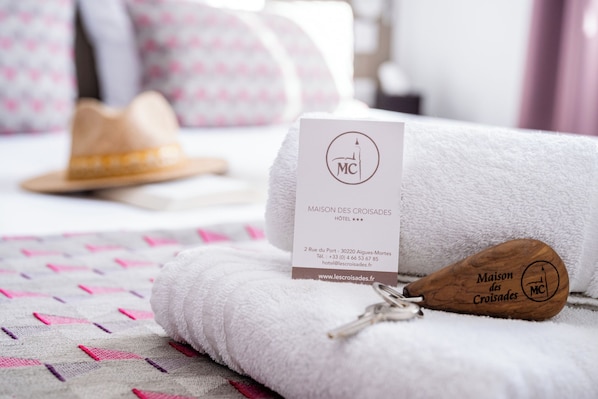 Habitación de hotel con una toalla blanca doblada con cuidado, un bastón de madera con el logotipo del hotel y una tarjeta de presentación sobre la toalla.