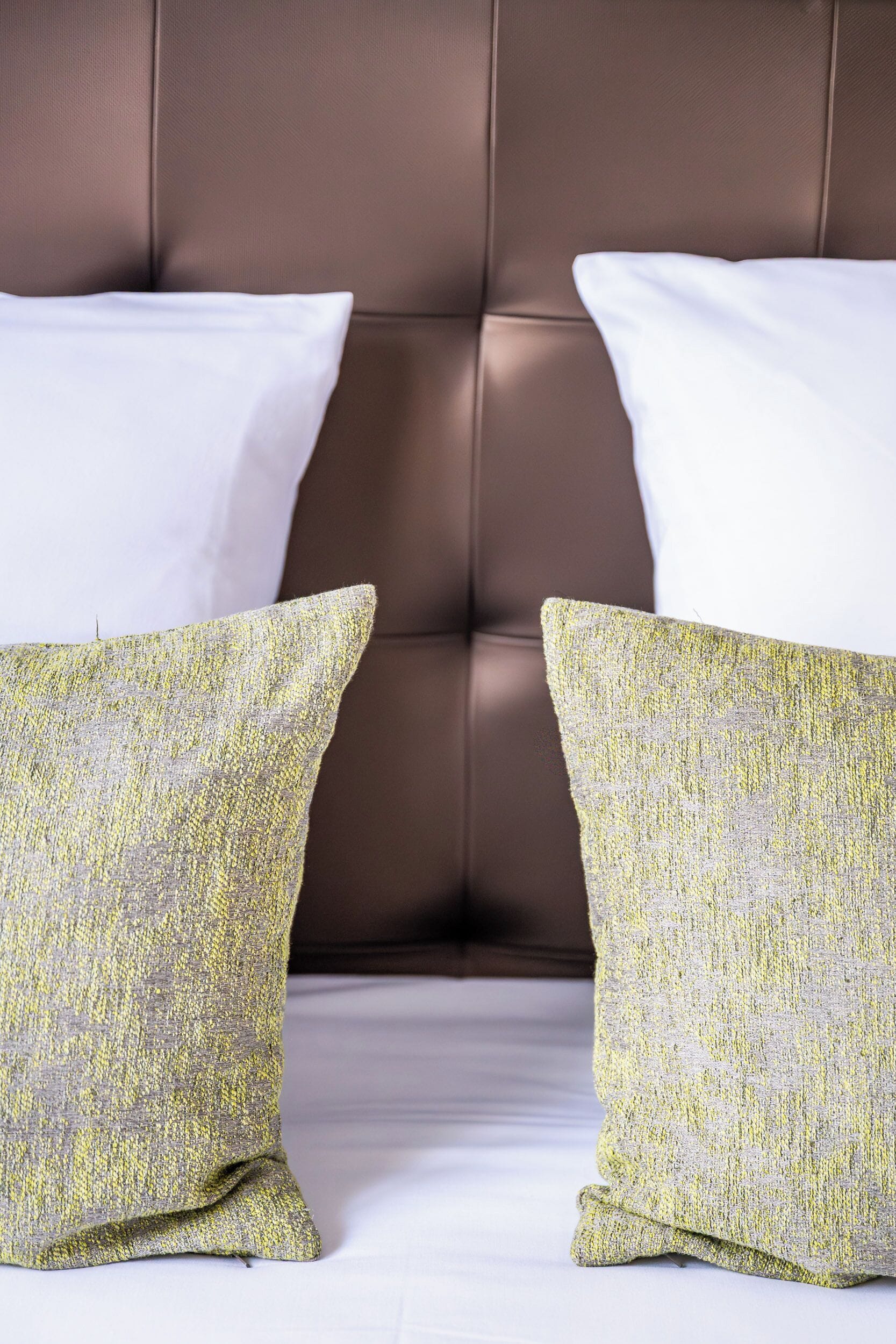 Una cama con dos almohadas, una blanca y otra amarilla, frente a un cabecero marrón.