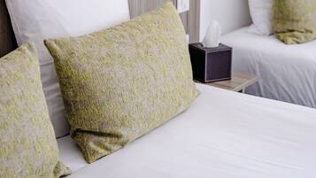 Una cama bien hecha con sábanas blancas y almohadas estampadas en verde, una lámpara de noche y una caja de pañuelos en la mesita de noche.