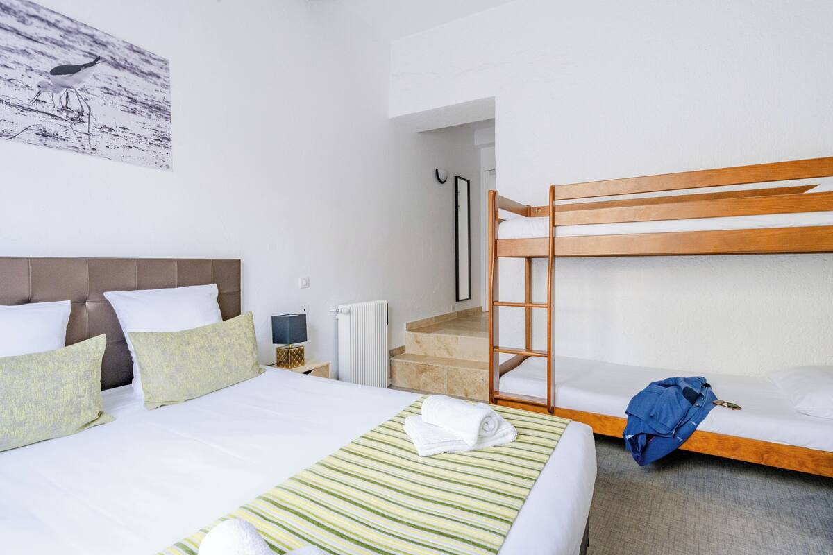 A hotel room with a bunk bed, a single bed, a green striped blanket, and a framed picture on the wall.