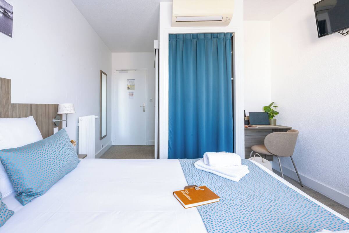 A hotel room with a bed, a desk, a chair, a TV, and a window with curtains.